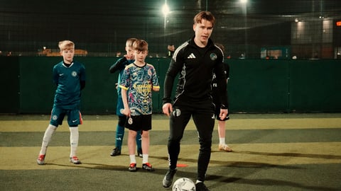 Soccer coach training young children on an outdoor field at night under stadium lights