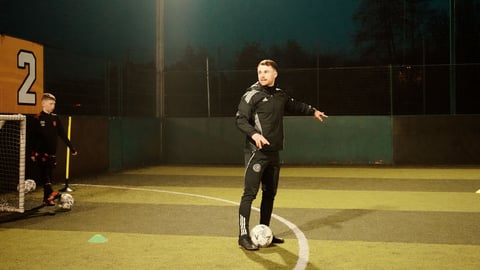 Soccer player in black uniform posing with ball on field at night under stadium lights