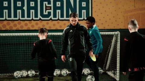 Coach instructing children during indoor soccer training session with nets and soccer balls visible